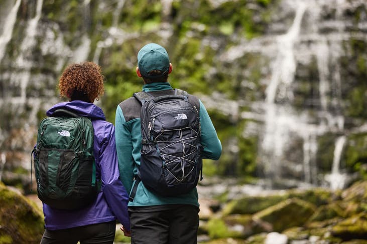 A couple in front of a waterfall with Th North Face backpacks